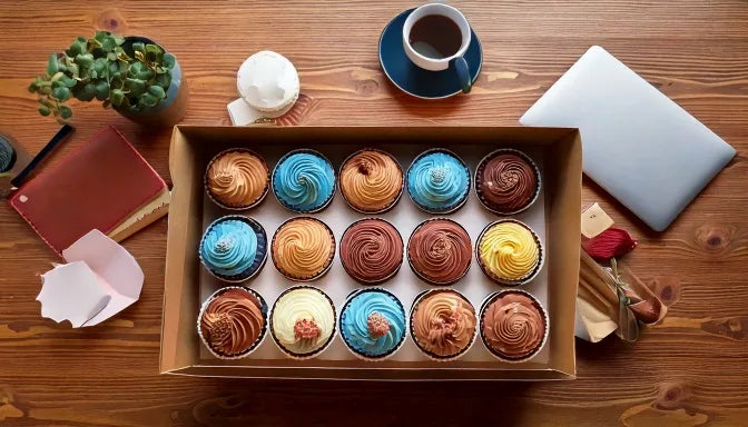 Overhead flat-lay of two dozen branded corporate cupcakes in a sleek box on a modern office conference table, uniform buttercream with round