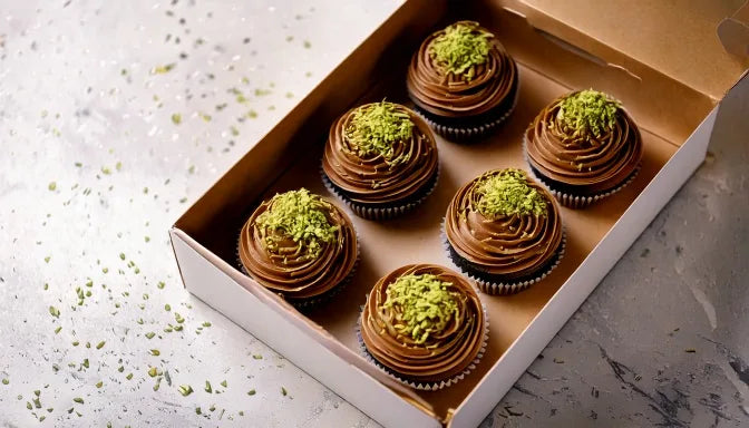 A box of Dubai chocolate cupcakes topped with pistachio cream, crushed kadayif, and milk chocolate drizzle