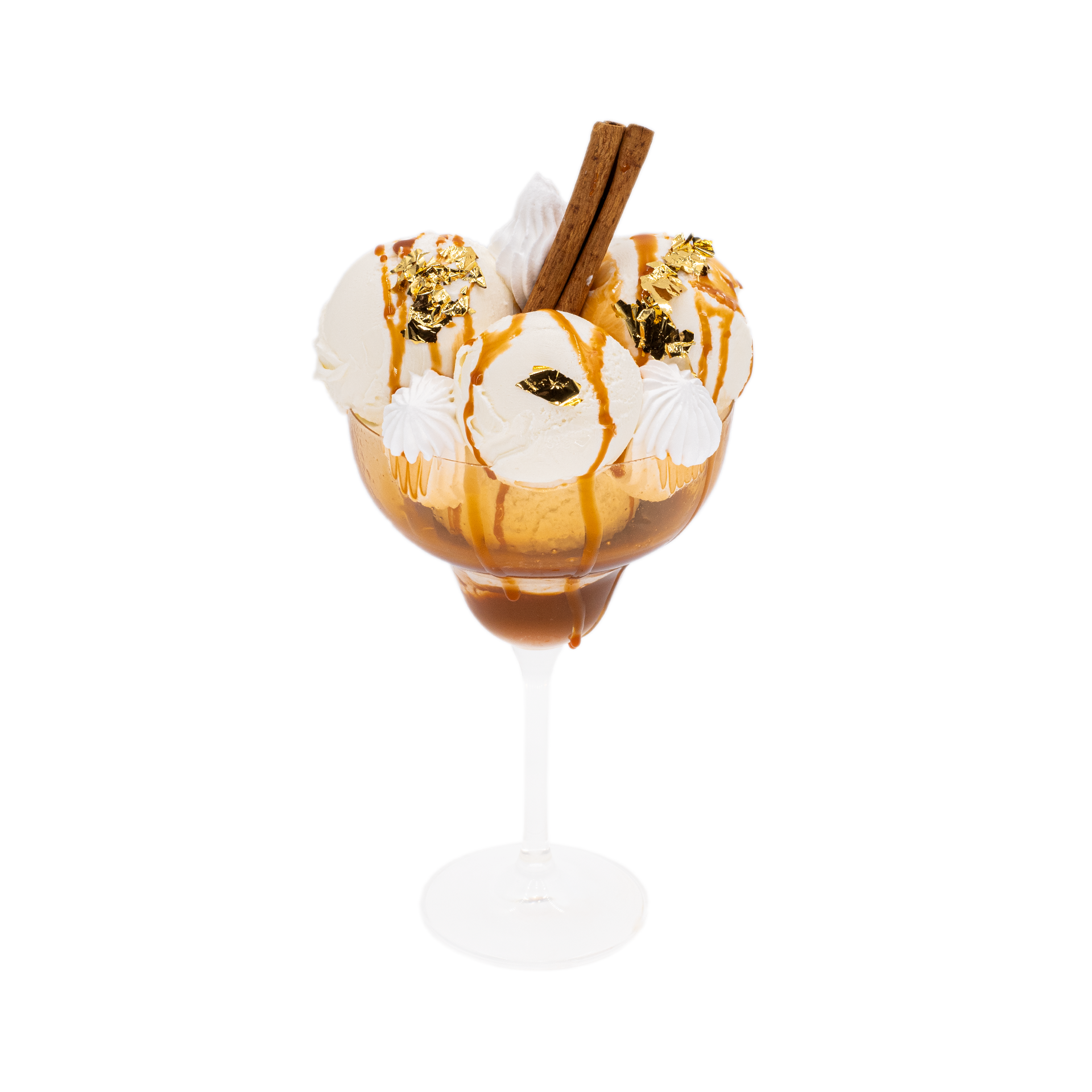 Gourmet ice cream sundae in glass with caramel drizzle, meringue, cinnamon sticks, and gold leaf