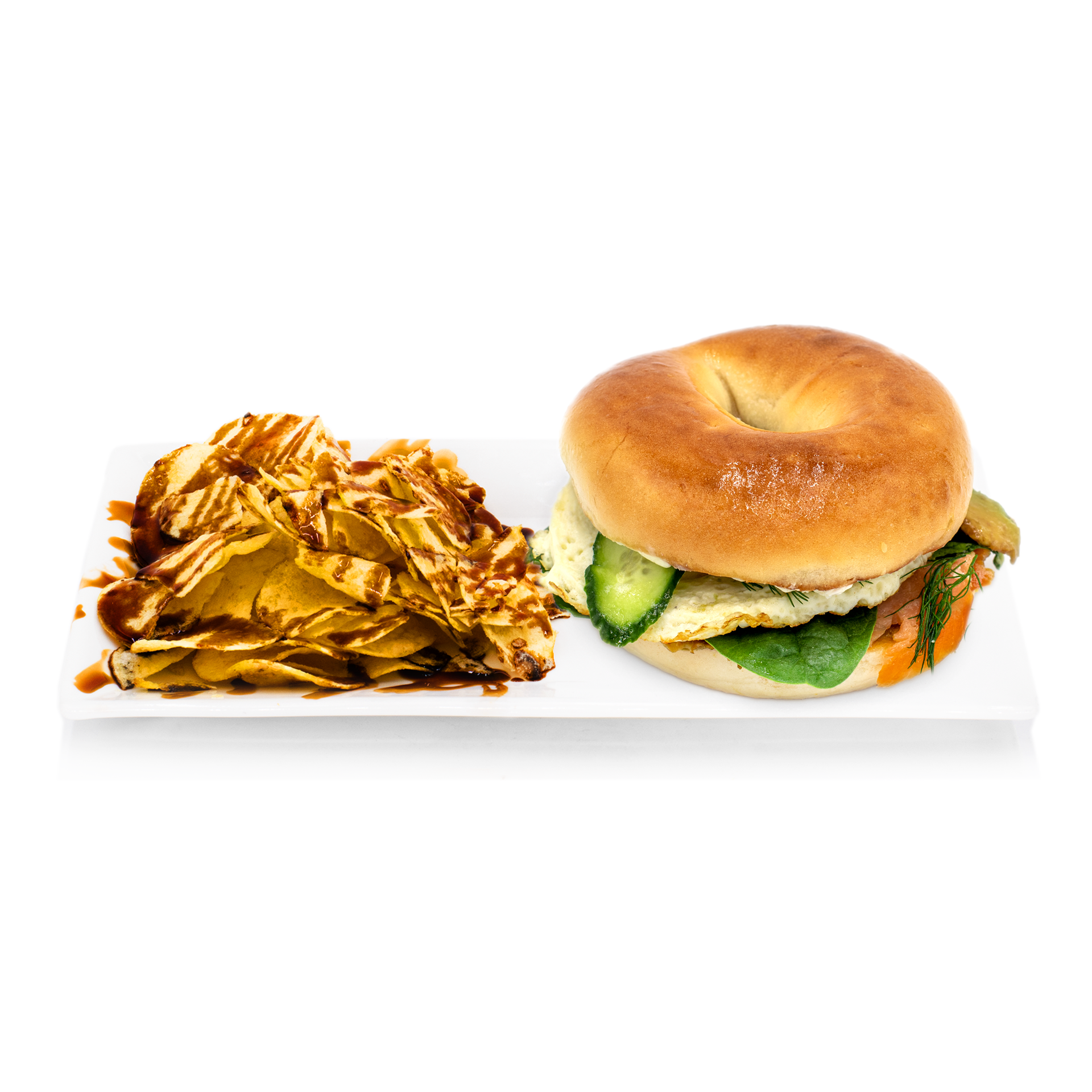 Bagel sandwich with egg, cucumber, greens, and chips drizzled with sauce on a white plate