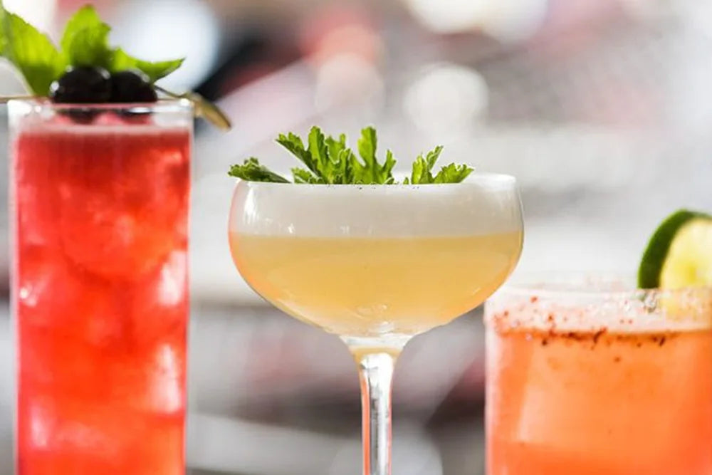 Assorted gourmet cocktails with fresh garnishes, including berries, mint, and lime