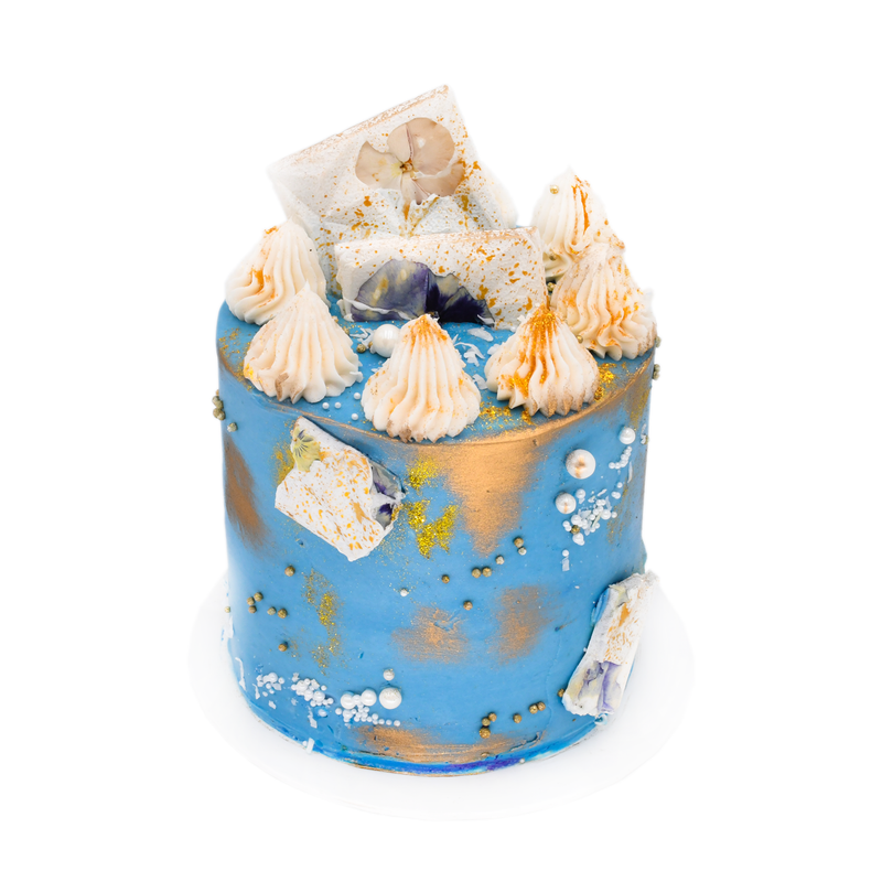Handcrafted blue and gold cake with meringue peaks, edible flowers, and decorative pearls
