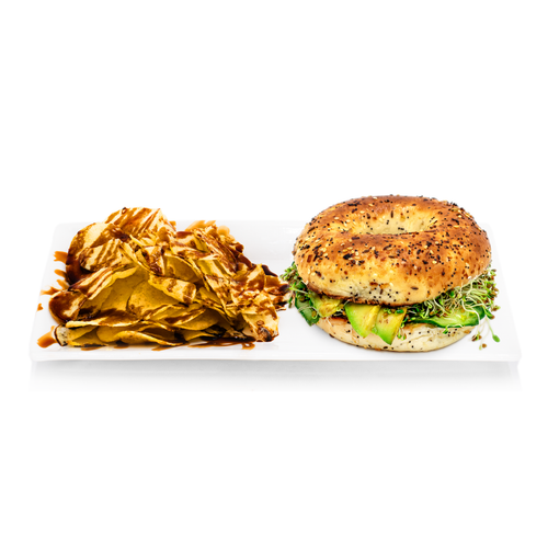 Everything bagel sandwich with avocado, sprouts and chips drizzled with sauce on a white plate