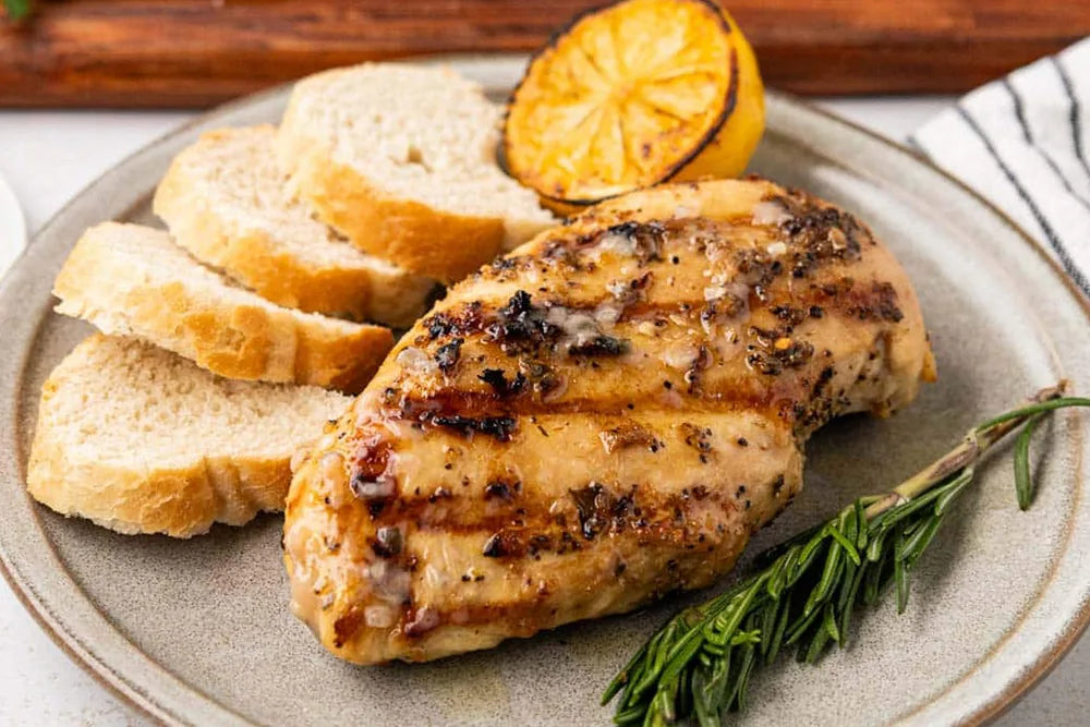 Grilled chicken breast with bread slices, lemon, and rosemary on a plate