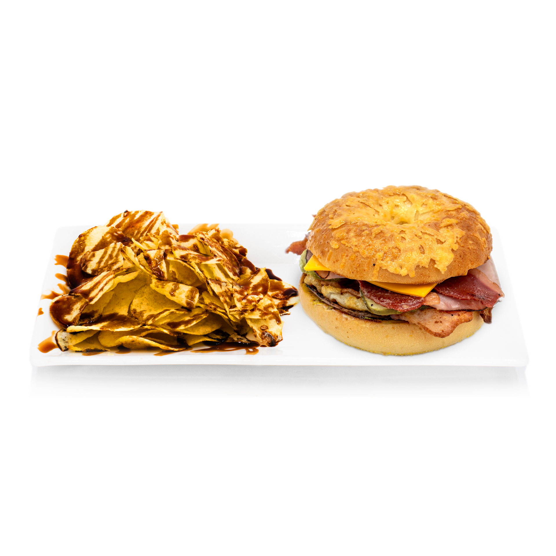 Gourmet sandwich with cheese and deli meats served on a bun, with potato chips drizzled in sauce.
