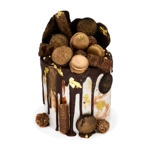 Chocolate drip cake topped with gold macarons, cookies, chocolate bars, and edible gold leaf