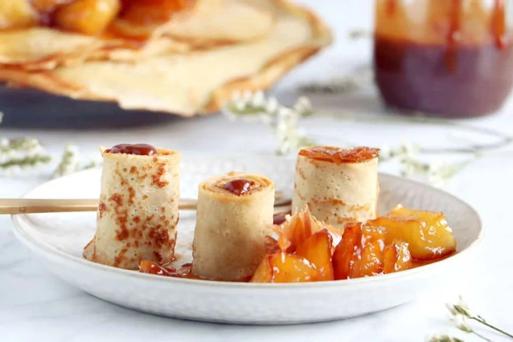 Rolled crepes with caramel sauce and caramelized fruit on a white plate