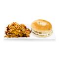 Bagel with cream cheese and chips drizzled with sauce on a white rectangular plate