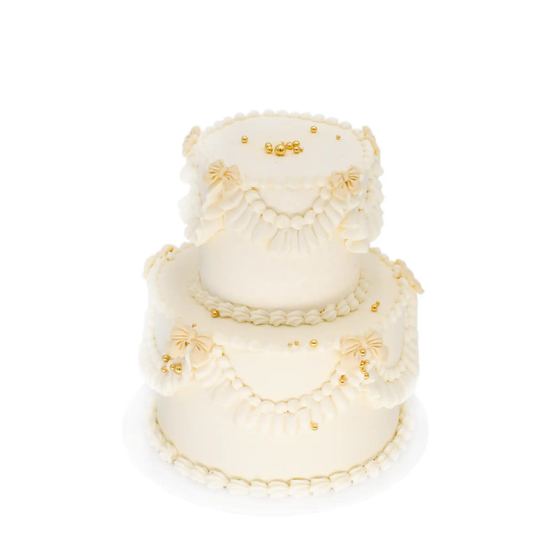 Two-tier white custom cake with gold accents and piped buttercream decorations