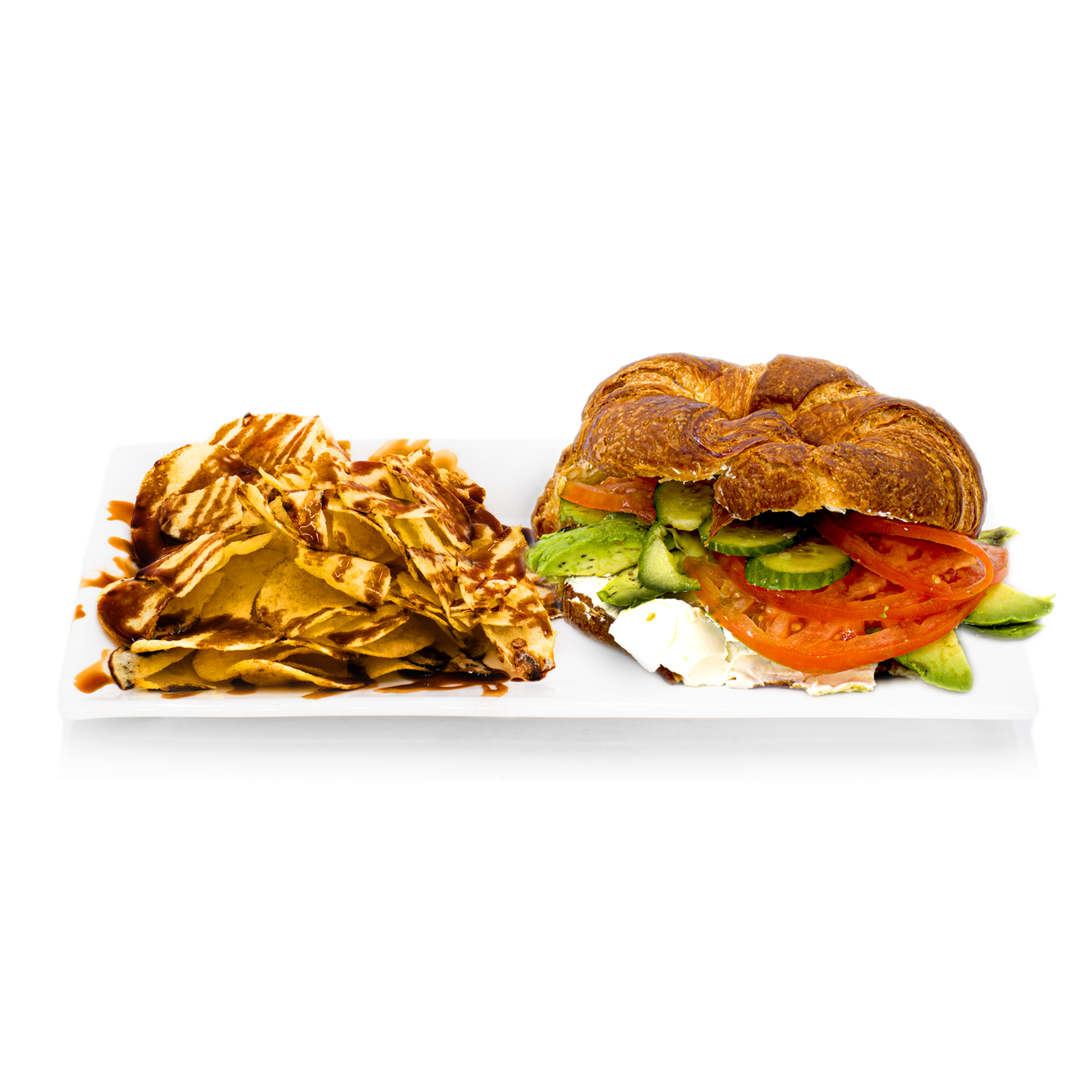 Croissant sandwich with tomato, avocado, and chips drizzled with sauce on white plate