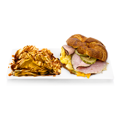 Ham and cheese croissant sandwich with pickles, served with potato chips and sauce on a white tray