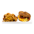 Croissant breakfast sandwich with bacon, eggs, cheddar cheese and side of potato chips drizzled with sauce