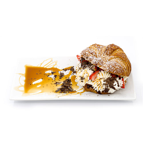 Gourmet breakfast croissant with whipped cream, chocolate shavings, strawberries, and caramel sauce.