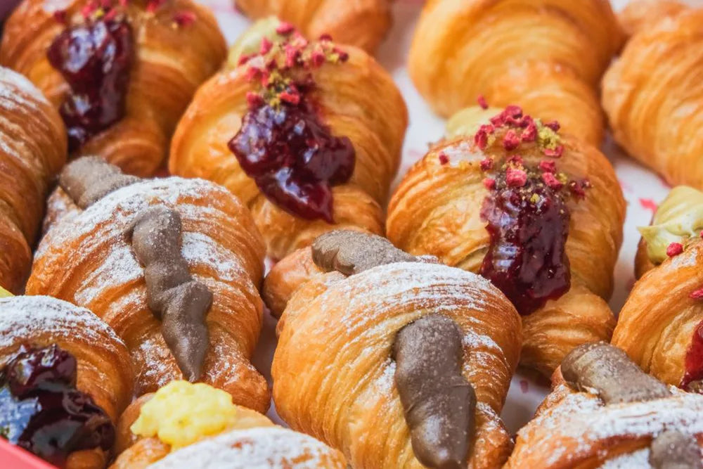 Assorted gourmet croissants filled with chocolate, jam, and cream, topped with powdered sugar.