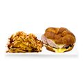 Croissant breakfast sandwich with ham, cheese, and eggs served with chips and sauce on a white plate