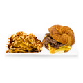 Croissant breakfast sandwich with eggs and meat, served with chips drizzled in sauce on white plate
