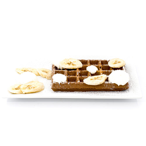 Chocolate waffle topped with banana slices and whipped cream on a white rectangular plate