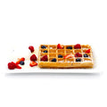 Golden waffle topped with fresh strawberries, blueberries, raspberries, powdered sugar, and whipped cream on a white plate