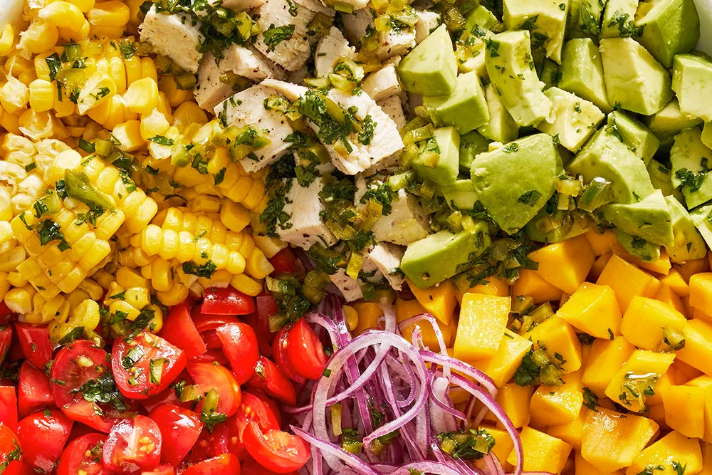 Fresh salad bowl with avocado, mango, corn, cherry tomatoes, red onion, and diced chicken.