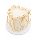 Heart Cloud Cake with smooth white frosting, decorated with elegant cream swirls, gold pearl accents, and soft gold satin ribbons tied in bows.