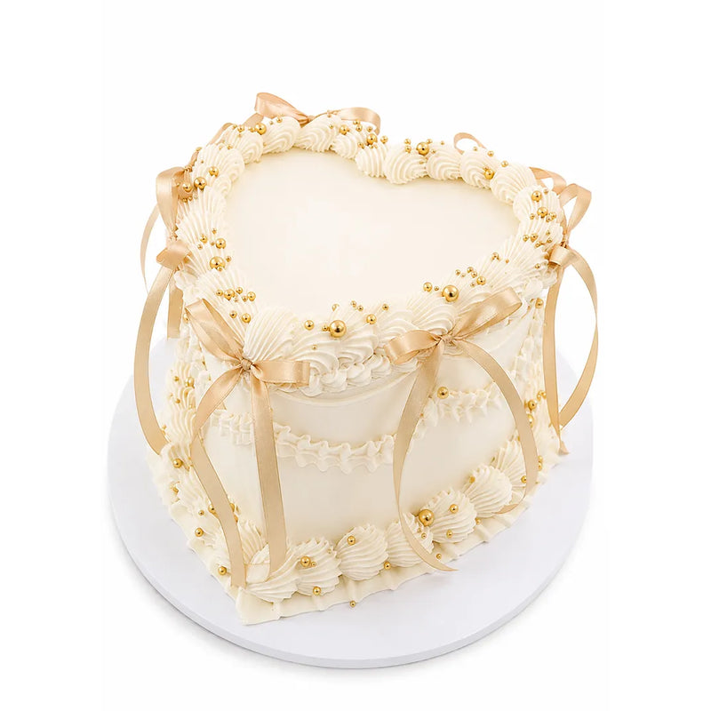 Heart Cloud Cake with smooth white frosting, decorated with elegant cream swirls, gold pearl accents, and soft gold satin ribbons tied in bows.