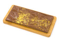 Milk chocolate bar with gold splatter on geometric pattern, displayed on wooden board