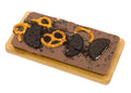 Milk chocolate bar topped with chocolate sandwich cookies and pretzels on a wooden board