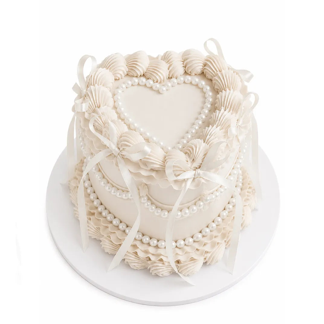 Pure Heart Cake with elegant white frosting, intricate piped details, heart-shaped center, pearl accents, and delicate ribbon decorations for a sophisticated celebration dessert.