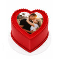 Red Love Story Heart Cake with smooth red icing, decorated with edible red beads, featuring a custom photo of a couple embracing on top, perfect for romantic celebrations.