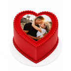 Red Love Story Heart Cake with smooth red icing, decorated with edible red beads, featuring a custom photo of a couple embracing on top, perfect for romantic celebrations.