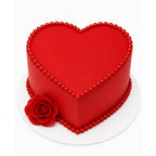 Red Love Story Rose Heart Cake in vibrant red with smooth finish, adorned with pearl-like bead borders and a realistic red rose on a white base, elegant custom cake.