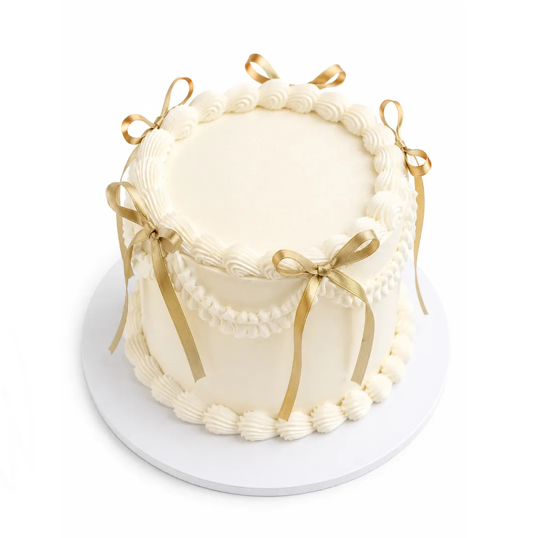 Soft Feelings Cake with smooth white frosting, decorated with piped borders and elegant gold ribbon bows, perfect for custom birthday cakes or luxury desserts.
