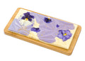 White chocolate bar with purple edible flowers and gold accents on wooden board