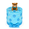 Baby Boy Cake featuring a blue frosted design with large blue polka dots, white sprinkles, a fondant bow at the base, and a sitting teddy bear topper for a charming celebration.