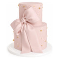 Two Tier Blush Bow Cake featuring a smooth pink fondant finish adorned with delicate gold and white edible pearls and a large elegant blush fondant bow, perfect for luxury celebrations.