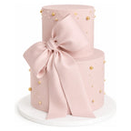 Two Tier Blush Bow Cake featuring a smooth pink fondant finish adorned with delicate gold and white edible pearls and a large elegant blush fondant bow, perfect for luxury celebrations.
