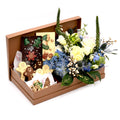 Gift box with assorted festive chocolates and cookies beside white and blue flower arrangement