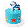 Ocean Adventure Cake featuring bright blue frosting decorated with white dots, seaweed, a red starfish, and toppers of a smiling shark and diver for a fun ocean theme.