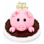 A pig-shaped cake with pink fondant ears, snout, and black eyes, sitting on a rich chocolate base with a gold "Happy Birthday" topper, called Piggy Mud Cake.