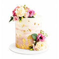 Elegant Golden Garden Cake featuring white and pink floral decorations with gold leaf accents on a smooth white and blush pink gradient icing, perfect for luxury celebrations.