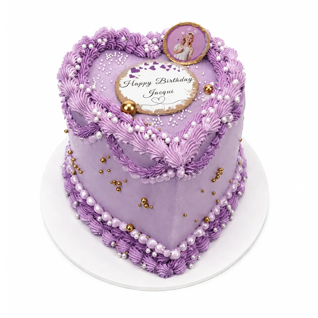 Purple Sparkle Heart Cake decorated with intricate lavender piping, pearl and gold edible beads, a personalized birthday message, and a small photo topper on a white base.