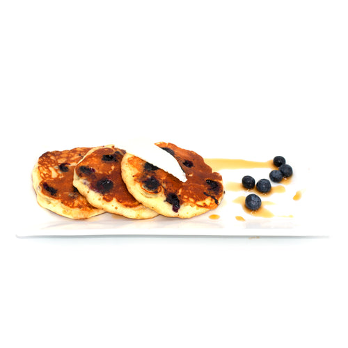 Blueberry pancakes topped with cream and maple syrup, served with fresh blueberries on a plate