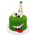 Little Monster Birthday Cake with bright green textured frosting, large playful eyes, a wide smiling mouth with white teeth, red tongue, and a colorful polka dot party hat.