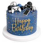 Blue birthday cake with gold speckled decoration topped with black, silver, and blue balls, and edible gaming-themed toppers including two controllers and a smartphone shape.