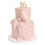 Two Tier Blush Bow Cake featuring a smooth blush pink finish adorned with gold pearl accents and a large matching bow, topped with gold number 16 decoration.
