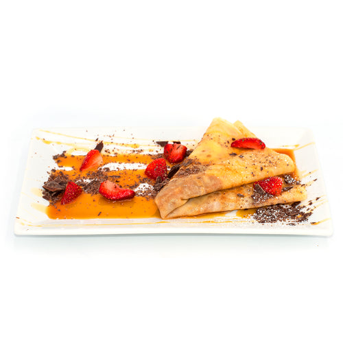 Caramel crepes with strawberries and chocolate shavings on a white plate