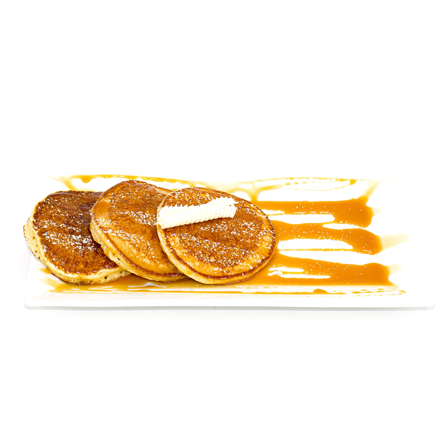 Three golden pancakes with butter and caramel sauce on a rectangular white plate