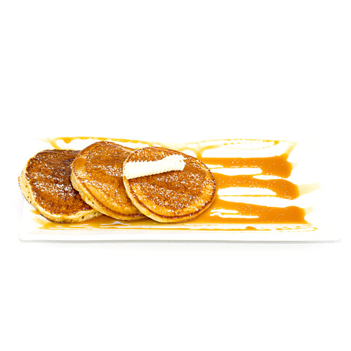 Three golden pancakes with butter and caramel sauce on a rectangular white plate