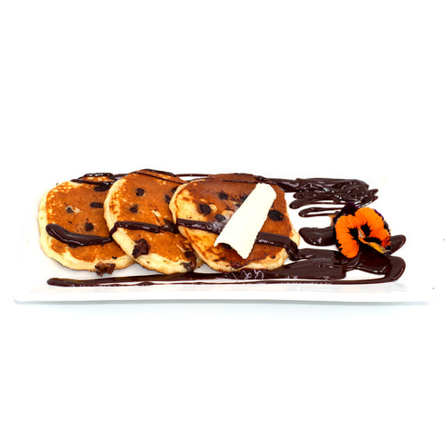 Chocolate chip pancakes with chocolate drizzle, butter, and edible flower on white plate