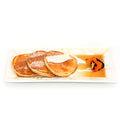 Three golden pancakes with powdered sugar, butter, syrup and edible flower on a white plate